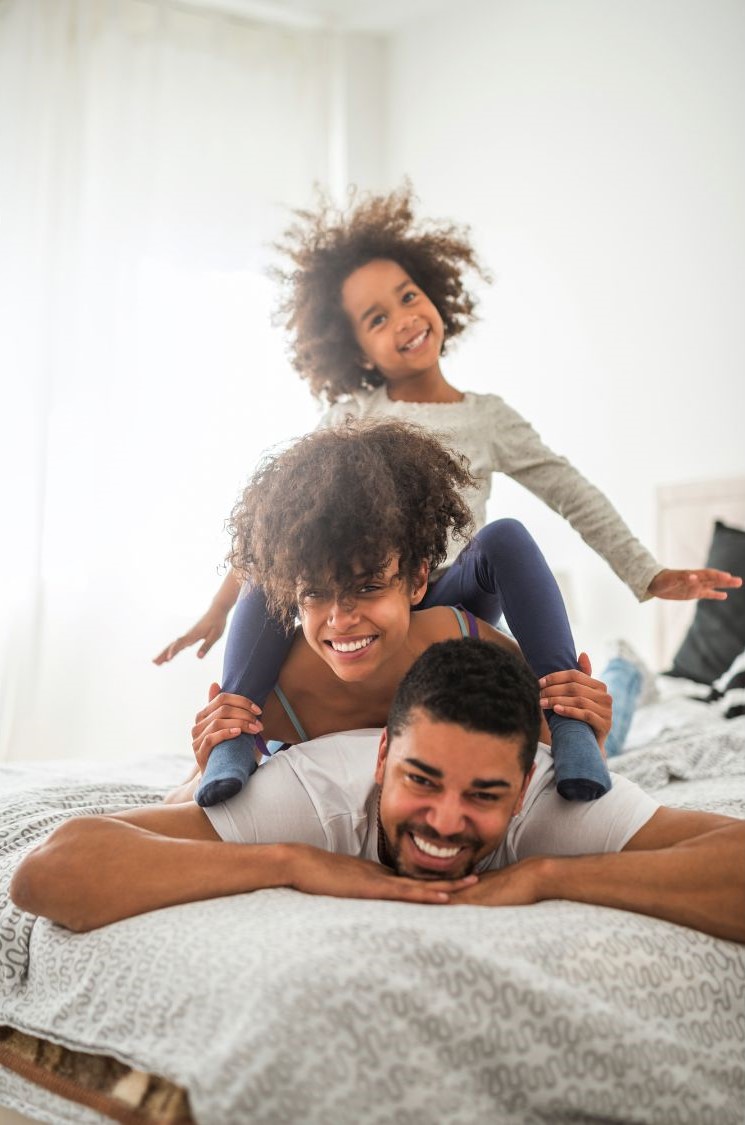 Happy family lying together on a bed. The family are laughing and joking whilst piling on the father.