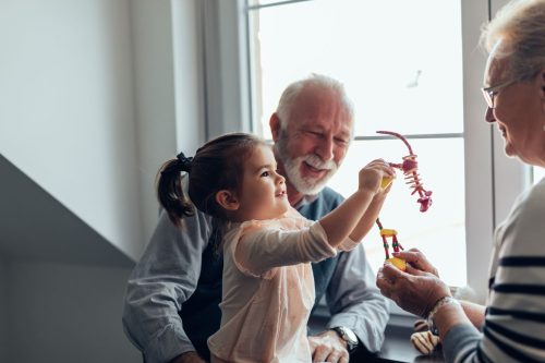 An image of grandparents playing with their granddaughter with her toys.