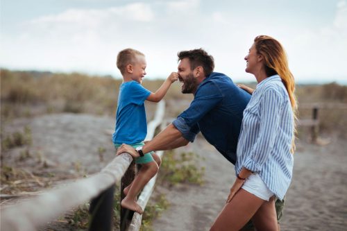 A couple laugh with their child as he is sat on a fence.