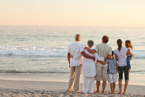 A family stood on the beach together, looking out to the sea while the sun starts to set.